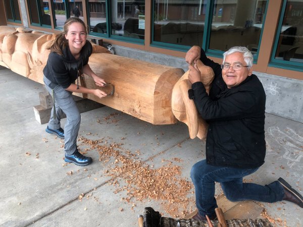 Carver Wayne Price and a student carve a pole