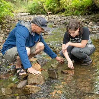 A teacher and student squatting in a forest creek
