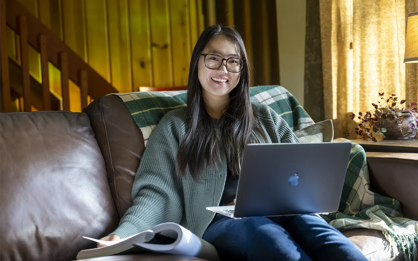 UAS student sitting on leather couch smiling with computer in lap