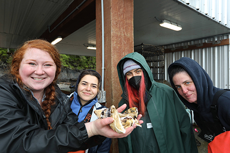 A group of students holds out some beautiful farmed oysters while visiting Hump Island Oyster Company offshore from Ketchikan.