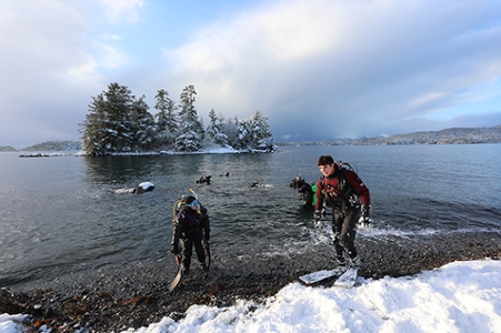 Scuba students enter the wintry waters from snowy shores at magic island in Sitka.