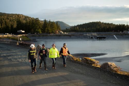 Four people walk along the water treatment pond at sunset.