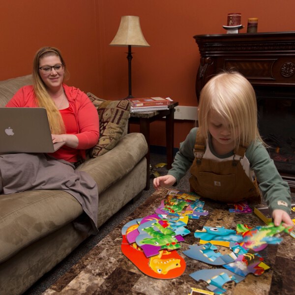 Woman on couch working on computer while child plays on the floor